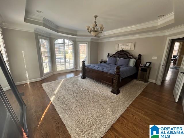 bedroom with baseboards, a raised ceiling, ornamental molding, dark wood-style flooring, and a chandelier