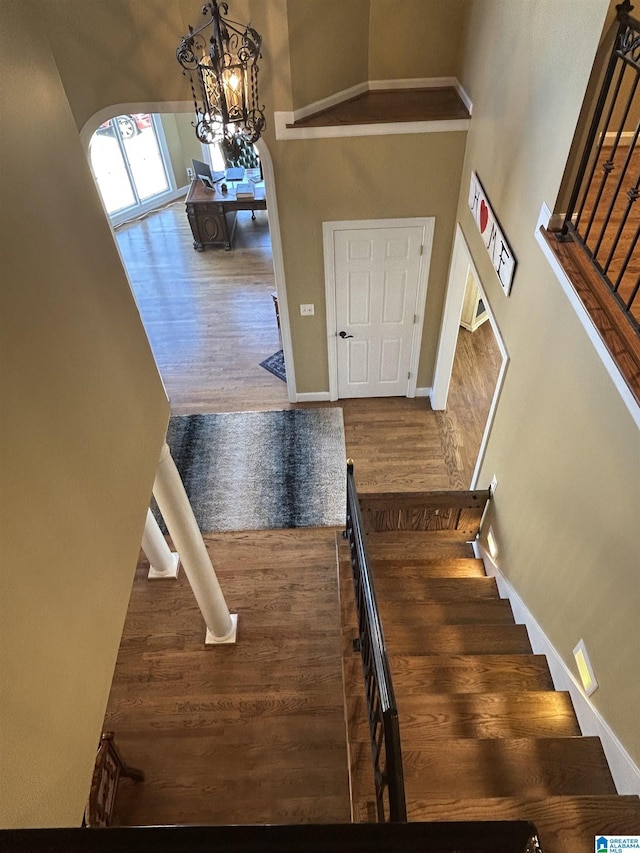 stairs featuring arched walkways, a chandelier, wood finished floors, and baseboards