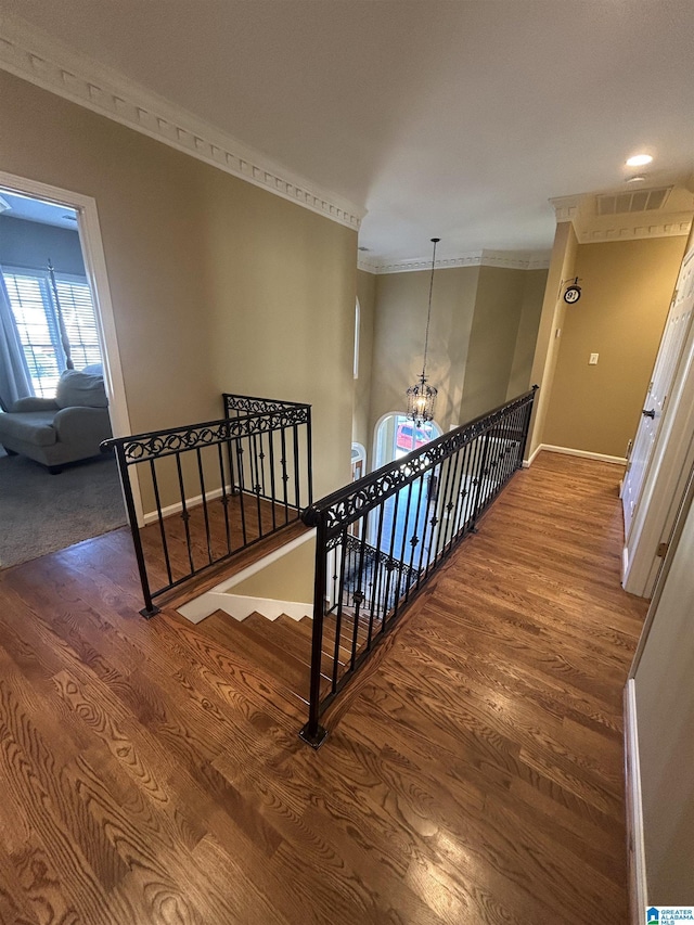 hallway featuring a chandelier, ornamental molding, wood finished floors, and an upstairs landing