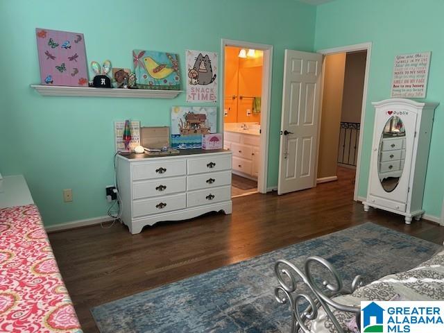 bedroom with ensuite bathroom, dark wood-style flooring, and baseboards