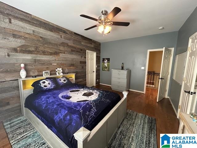 bedroom with wooden walls, an accent wall, wood finished floors, a ceiling fan, and baseboards