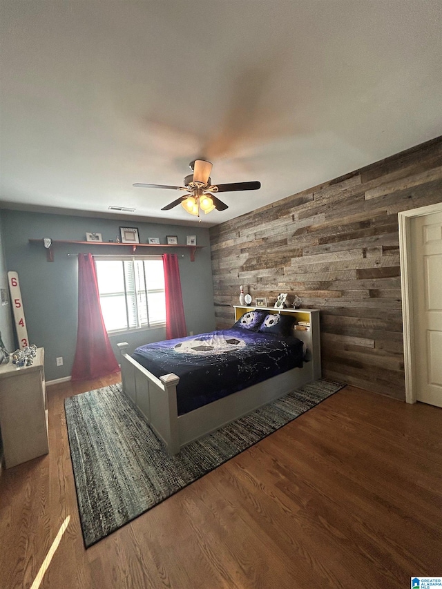 bedroom featuring a ceiling fan, wood finished floors, visible vents, and wooden walls