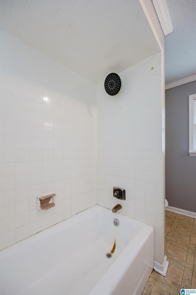 full bathroom featuring toilet, ornamental molding, stone finish floor, a textured ceiling, and baseboards