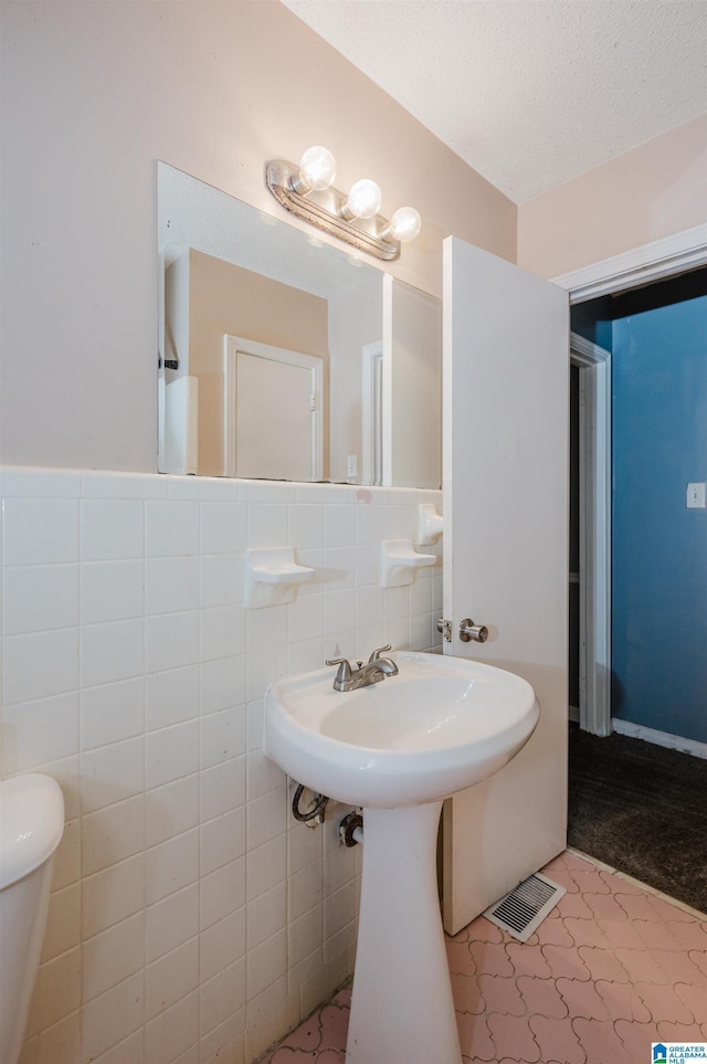 half bath with tile walls, visible vents, toilet, wainscoting, and a textured ceiling