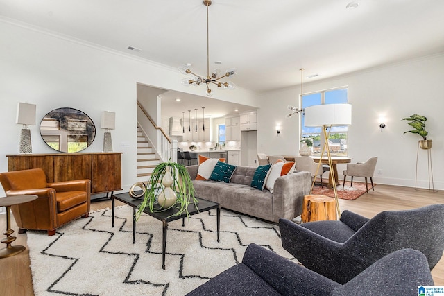 living room with visible vents, stairs, ornamental molding, light wood finished floors, and an inviting chandelier