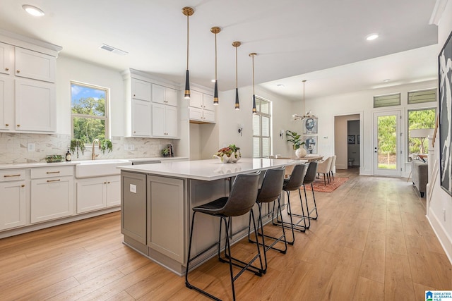 kitchen with visible vents, a kitchen island, light countertops, white cabinetry, and a sink