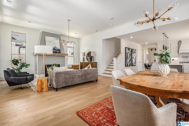 dining area with an inviting chandelier, ornamental molding, light wood-type flooring, a lit fireplace, and stairs