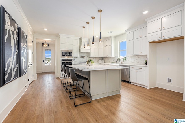 kitchen featuring white cabinets, appliances with stainless steel finishes, a center island, hanging light fixtures, and light countertops