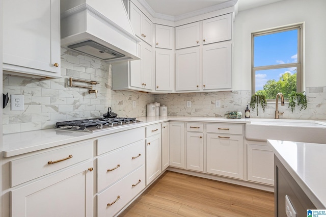 kitchen with stainless steel gas cooktop, light countertops, white cabinetry, and custom range hood