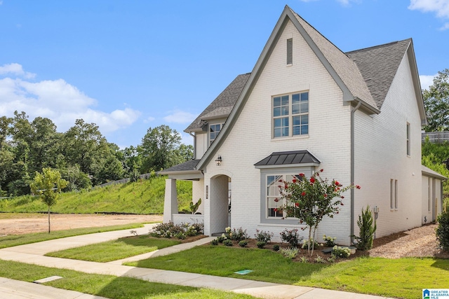 view of front of property with a shingled roof, a front yard, and brick siding