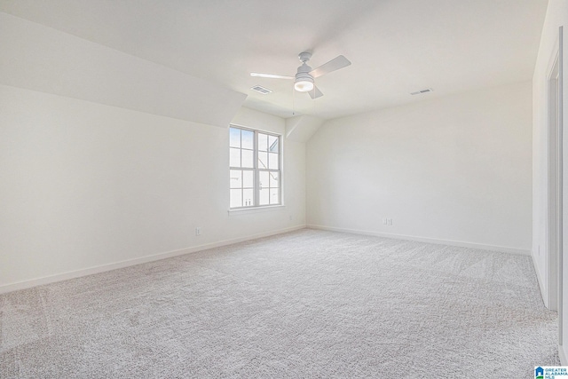 carpeted spare room featuring ceiling fan, vaulted ceiling, visible vents, and baseboards