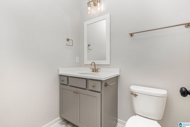 half bath with toilet, marble finish floor, baseboards, and vanity