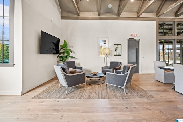 interior space with baseboards, beamed ceiling, a towering ceiling, and light wood finished floors