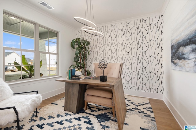 office area with an accent wall, wood finished floors, visible vents, baseboards, and crown molding