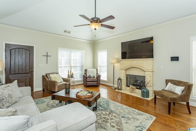 living area featuring a fireplace, visible vents, ornamental molding, ceiling fan, and wood finished floors