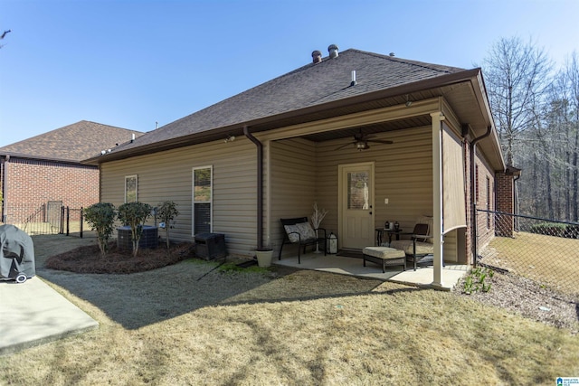 rear view of house with a lawn, ceiling fan, roof with shingles, fence, and a patio area