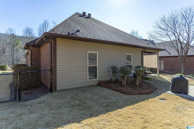 back of property with a shingled roof, a yard, brick siding, and fence