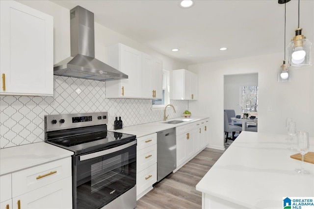 kitchen with a sink, white cabinetry, appliances with stainless steel finishes, wall chimney exhaust hood, and decorative light fixtures