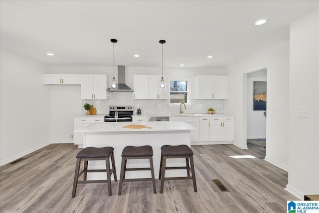 kitchen with a kitchen island, light countertops, stainless steel range with electric cooktop, wall chimney range hood, and white cabinetry