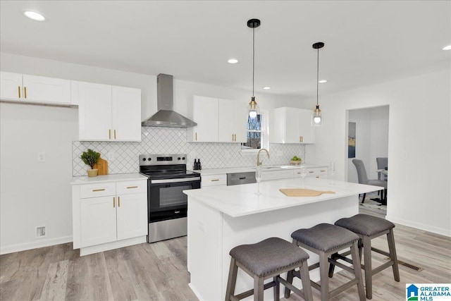 kitchen featuring a kitchen island, white cabinets, hanging light fixtures, stainless steel electric range oven, and wall chimney exhaust hood