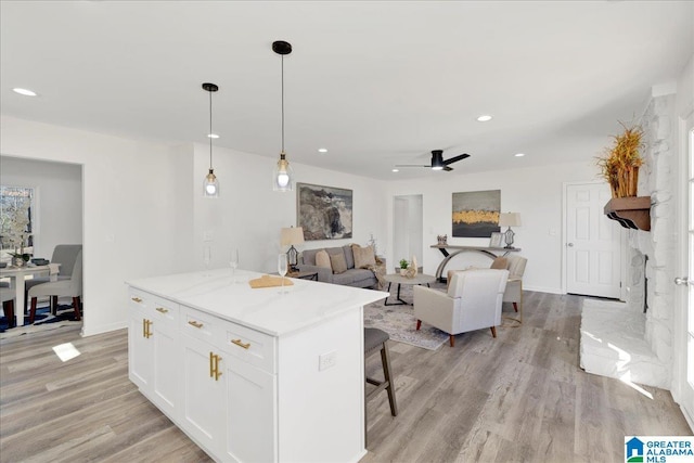 kitchen featuring decorative light fixtures, open floor plan, white cabinets, a kitchen island, and light wood-type flooring