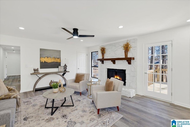 living area featuring recessed lighting, ceiling fan, a stone fireplace, wood finished floors, and baseboards