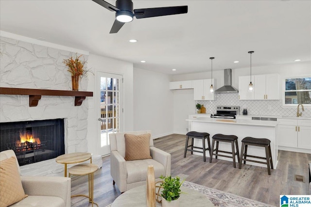 living area with light wood finished floors, recessed lighting, a ceiling fan, and a stone fireplace