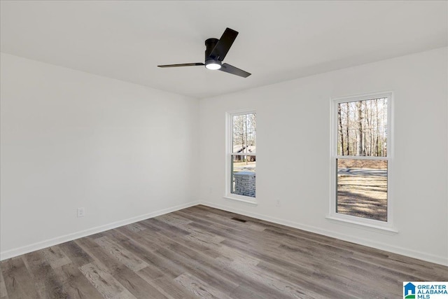 spare room featuring baseboards, light wood-type flooring, visible vents, and a healthy amount of sunlight