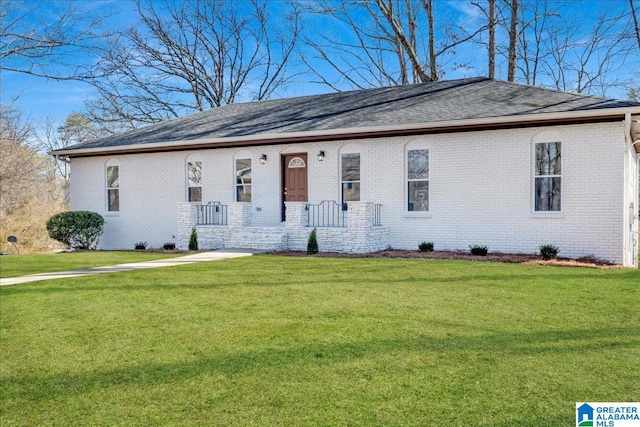 single story home featuring a shingled roof, a front yard, and brick siding