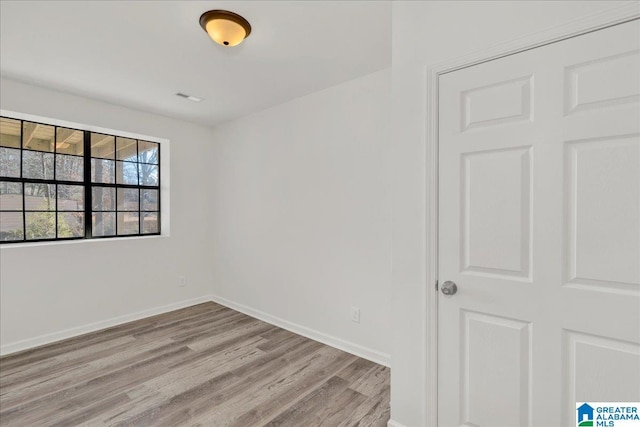 empty room featuring light wood-style floors, visible vents, and baseboards