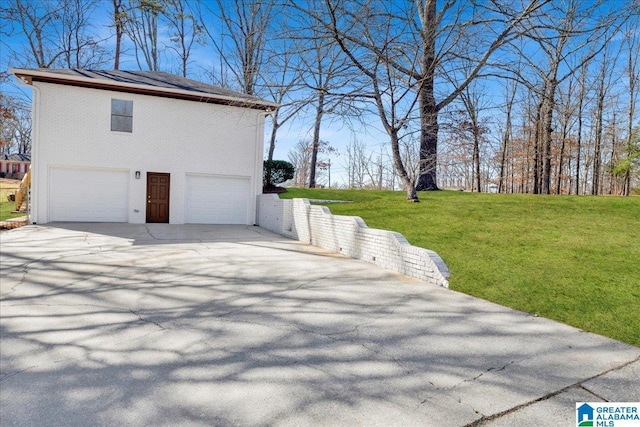 view of side of home with a yard, brick siding, an attached garage, and driveway