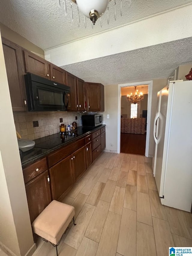 kitchen featuring wood tiled floor, black appliances, tasteful backsplash, dark countertops, and an inviting chandelier