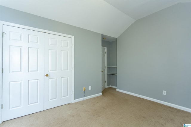 unfurnished bedroom with lofted ceiling, a closet, carpet flooring, and baseboards