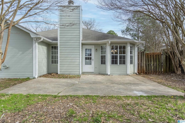 exterior space with a shingled roof, a patio, a chimney, and fence