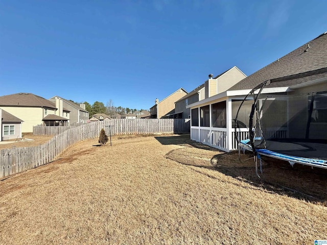 view of yard with a sunroom, a fenced backyard, a trampoline, and a residential view