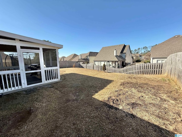 view of yard featuring a sunroom, a fenced backyard, and a residential view