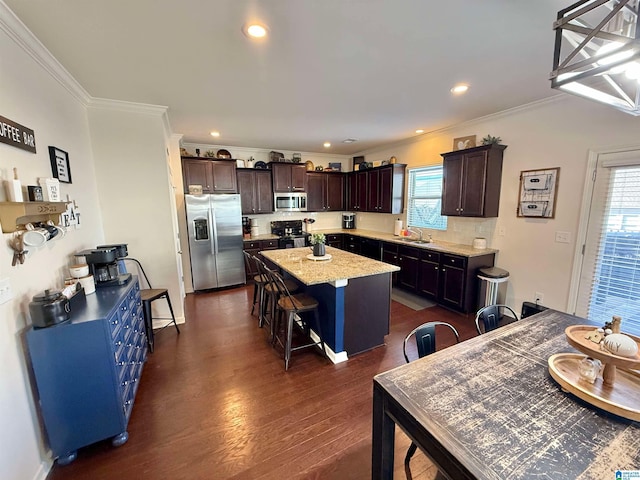 kitchen with a sink, a kitchen island, dark brown cabinets, appliances with stainless steel finishes, and a kitchen bar