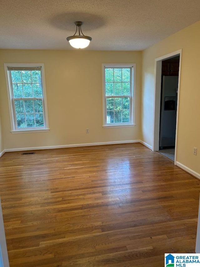 unfurnished room featuring visible vents, a textured ceiling, baseboards, and wood finished floors