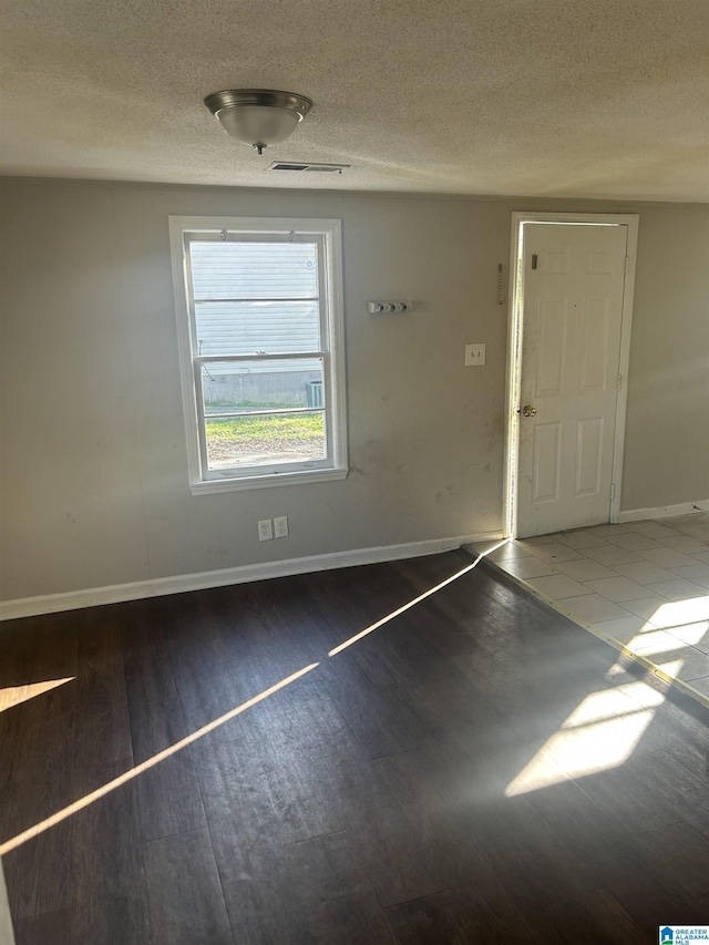 spare room with a textured ceiling, dark wood finished floors, visible vents, and baseboards