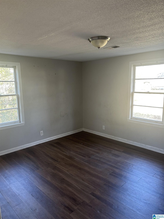 unfurnished room with a textured ceiling, dark wood-type flooring, visible vents, and baseboards