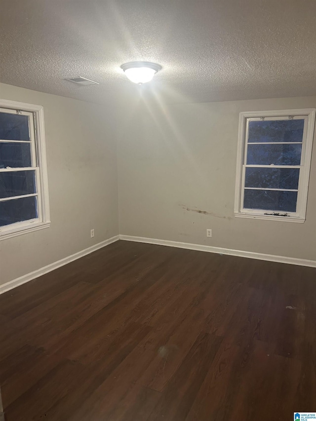 empty room featuring a textured ceiling, baseboards, and dark wood-type flooring