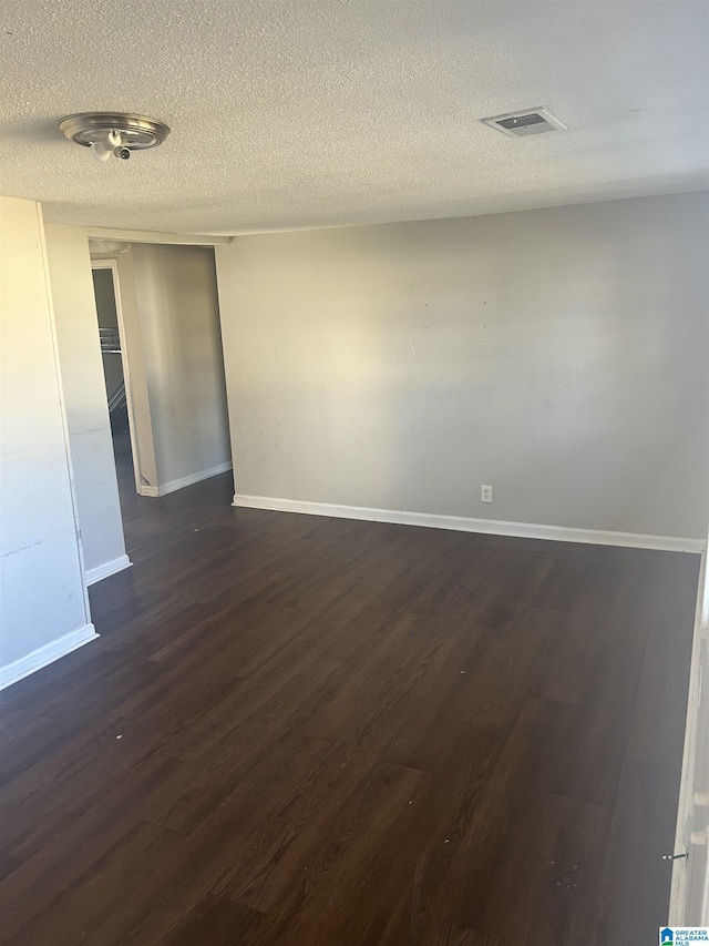 spare room with a textured ceiling, dark wood-type flooring, visible vents, and baseboards