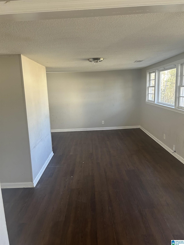 unfurnished room featuring baseboards, dark wood finished floors, and a textured ceiling