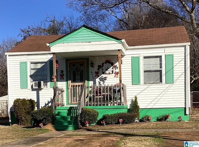 bungalow with a porch, cooling unit, and roof with shingles