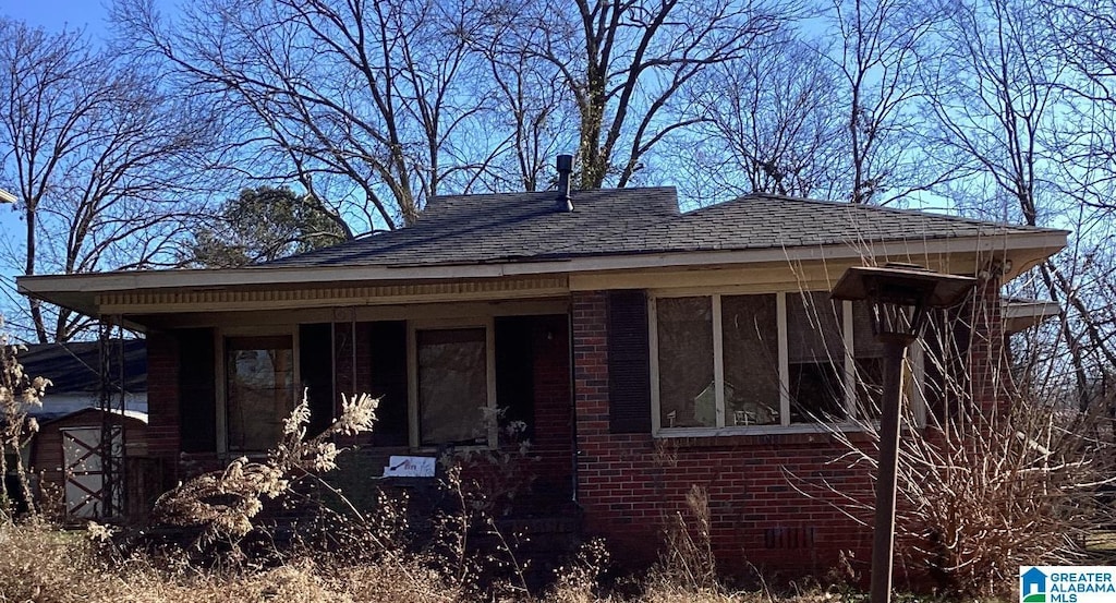 view of front facade featuring roof with shingles and brick siding