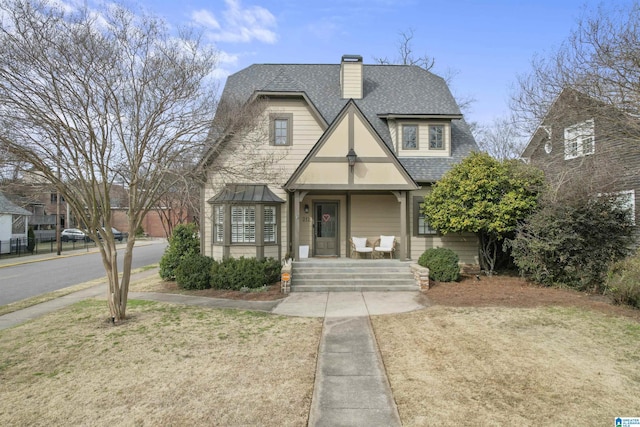 tudor house with a front yard, a chimney, and roof with shingles