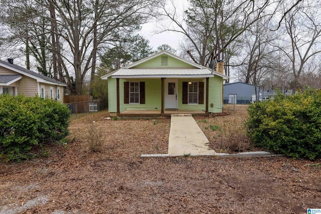 bungalow with covered porch, a chimney, fence, and metal roof