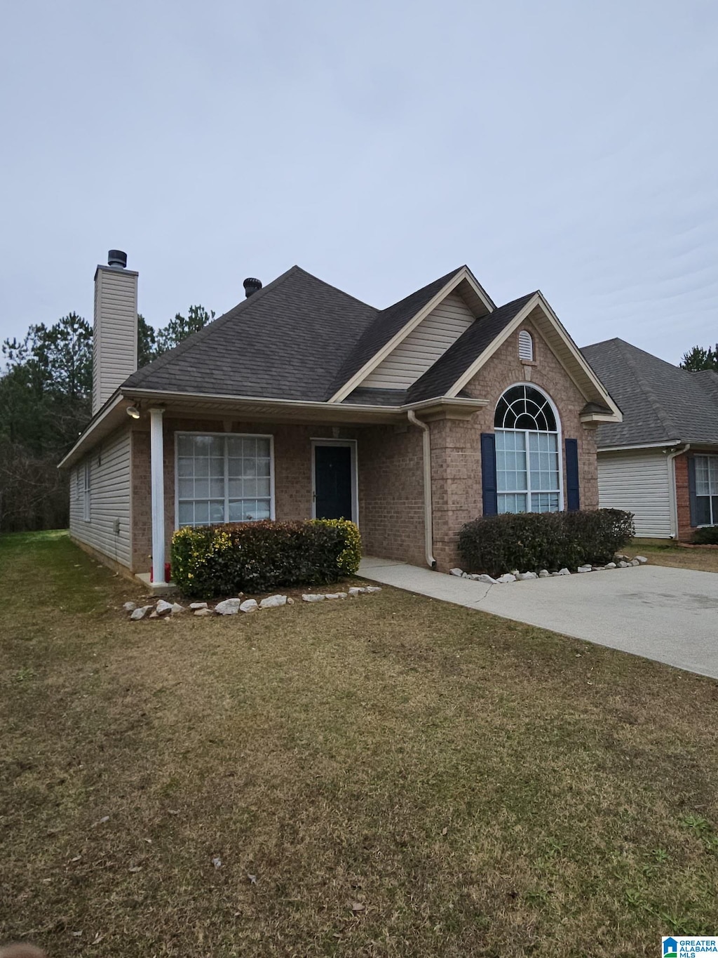 ranch-style home with roof with shingles, a front yard, a chimney, and brick siding