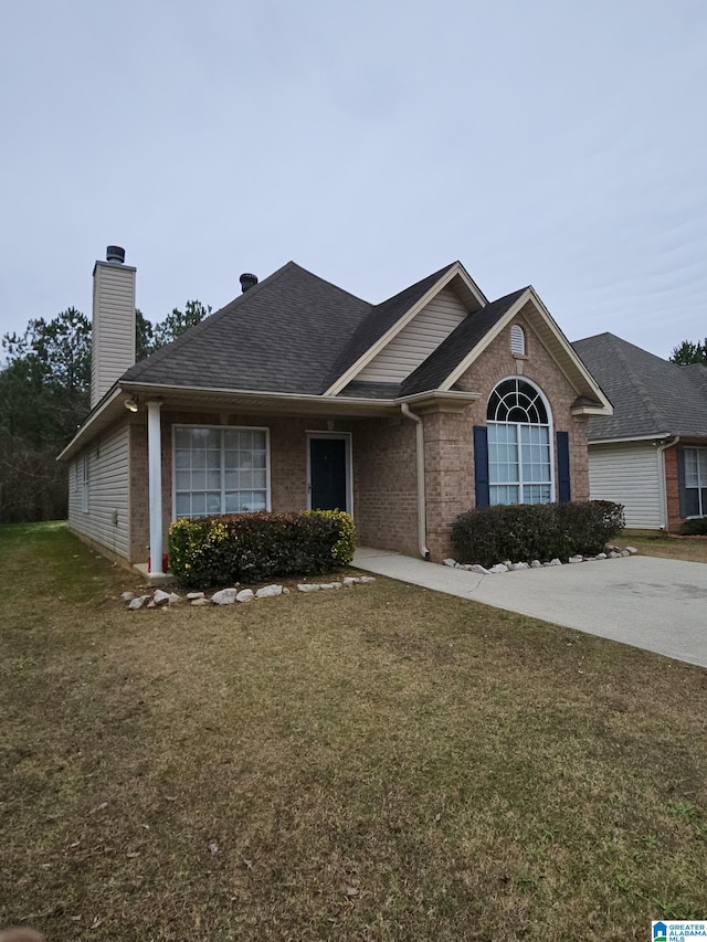 ranch-style home with roof with shingles, a front yard, a chimney, and brick siding