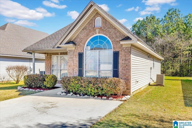 view of front of house with a front lawn, central AC unit, brick siding, and roof with shingles